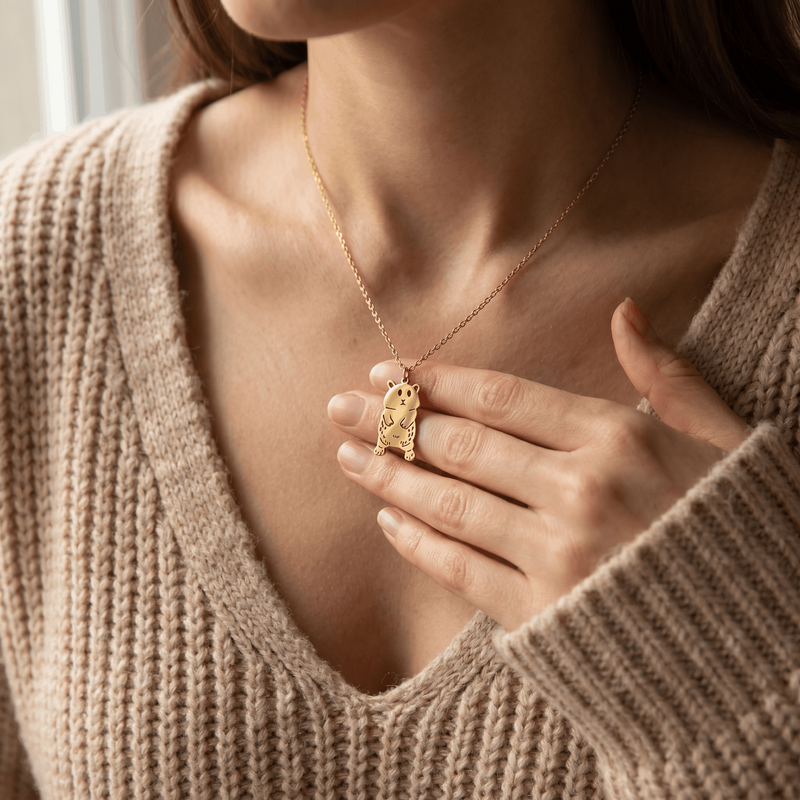 Frau im beigen Strickpullover trägt goldfarbene Kinderzeichnung-Halskette mit ausgestanztem Tier-Anhänger aus Edelstahl (KI-Visualisierung)