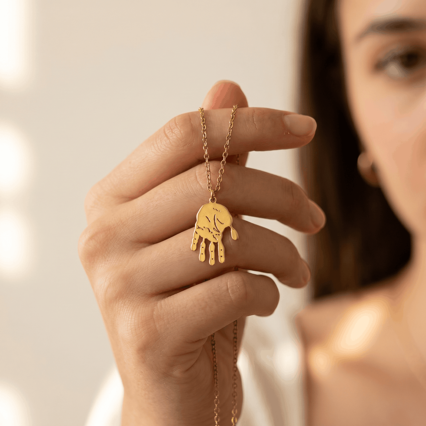 Frau hält goldfarbene Handabdruck-Halskette mit ausgestanztem Baby-Handabdruck-Anhänger aus Edelstahl zwischen den Fingern